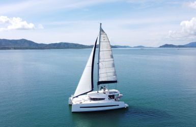 Catamaran zeilt over water met heuvelachtig land op de achtergrond