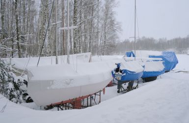 Zeilboten in winterstalling, afgedekt en bedekt met sneeuw